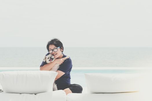 Asian woman and dog happy smile hugging on white beach bed at outdoor swimming pool seaside turquoise sea or ocean with horizon of blue sky at resort or hotel when vacation travel for relax