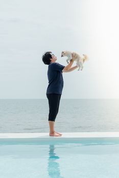 Asian woman and dog happy smile hugging at outdoor swimming pool seaside turquoise sea or ocean with horizon of blue sky at resort or hotel when vacation travel for relax