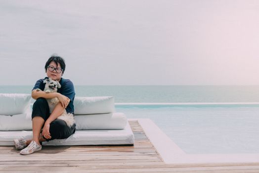 Asian woman and dog happy smile hugging on white beach bed at outdoor swimming pool seaside turquoise sea or ocean with horizon of blue sky at resort or hotel when vacation travel for relax