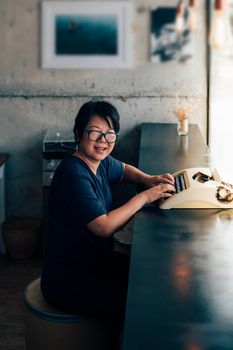 Asian woman 40s white skin with eyeglass sitting for writing something by vintage typewriter in a coffee shop cafe