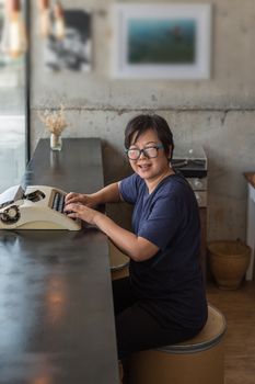 Asian woman 40s white skin with eyeglass sitting for writing something by vintage typewriter in a coffee shop cafe