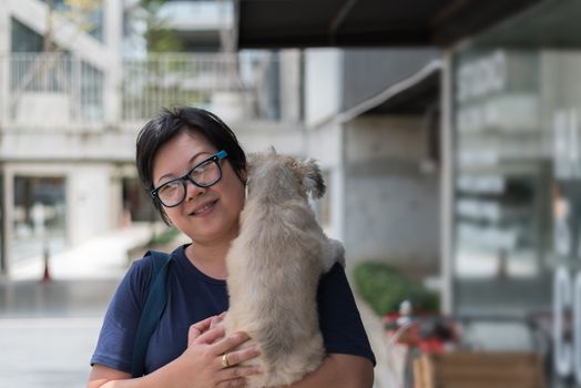 Asian woman and dog happy smile hugging her pat is a dog so cute mixed breed with Shih-Tzu, Pomeranian and Poodle at coffee shop cafe or restaurant with copy space
