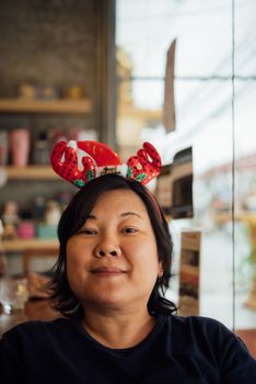 Asian woman 40s white skin have a laughing smile gesture in a coffee shop cafe with santa claus headband in merry christmas and new yaer celebration