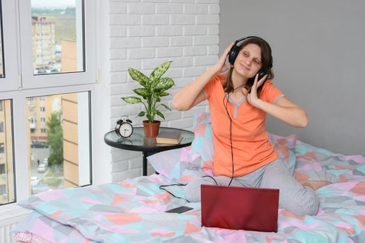 Girl listening to a lecture in headphones sitting at home on the bed