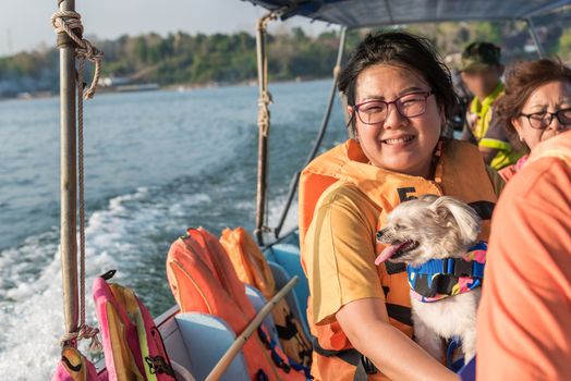 Asian woman and dog so cute mixed breed with Shih-Tzu, Pomeranian and Poodle sailing on Songkaria river by long tail boat with sun light in evening time when vacation travel for relax