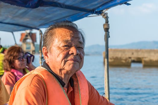 Asian elderly man sailing on Songkaria river by long tail boat with sun light in evening time when vacation travel for relax