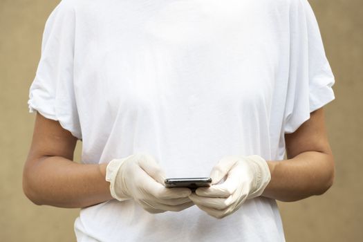 Woman wearing protective gloves and texting or chatting with her Smartphone. Close-up on hands, natural lighting and copy space on womans' t-shirt