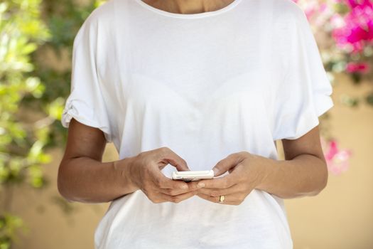 Woman in the forty's using a smartphone with white t-shirt for background or presentation, with large copy space and flowers background