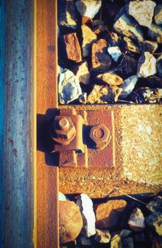 Close up and macro outdoor view of a rusty bolt and screw nut next to a rusty rail steel beam and stones next to the railway. 