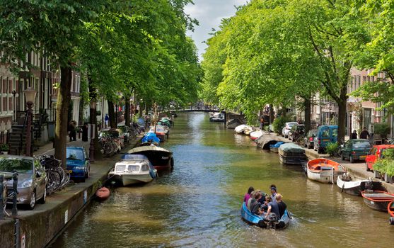 AMSTERDAM, NETHERLANDS - MAY 30: Amsterdam canals on May 30, 2014 in Amsterdam, Netherlands. View of Amsterdam canals and typical dutch houses.

Amsterdam, Netherlands - May 30, 2014: View of Amsterdam canals and typical dutch houses. People are travelling on the boat.