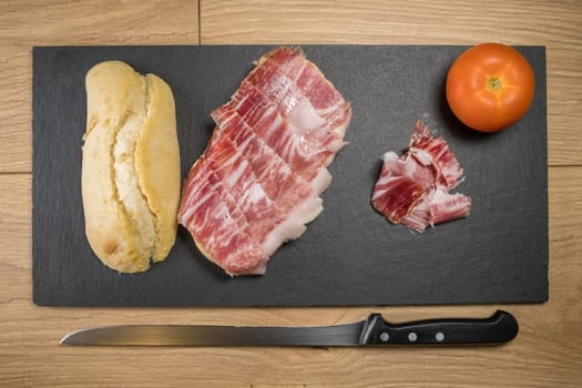 Iberian acorn ham sandwich with its knife, tomato and garlic. Spanish typical tapas