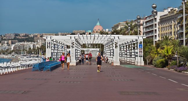NICE, FRANCE - JUNE 6, 2014: Pedestrians walking on Promenade des Anglais. Promenade des Anglais is a symbol of the Cote d'Azur and was built in 1830 at the expense of the British colony.

Nice, France - June 6, 2014: Pedestrians walking on Promenade des Anglais. Promenade des Anglais is a symbol of the Cote d'Azur and was built in 1830 at the expense of the British colony. People are resting and are walking.
