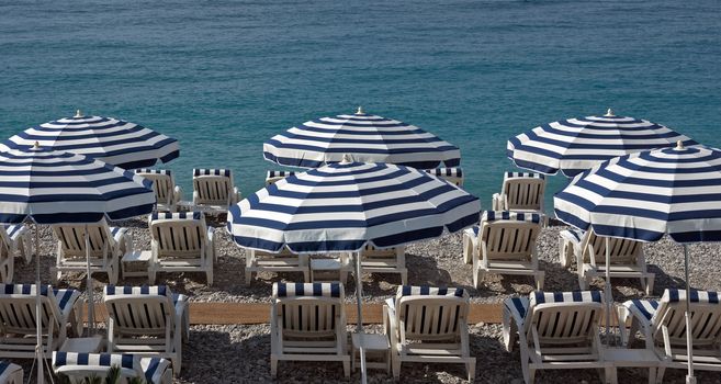 Beach with blue umbrellas near Promenade des Anglais in city of Nice, France.