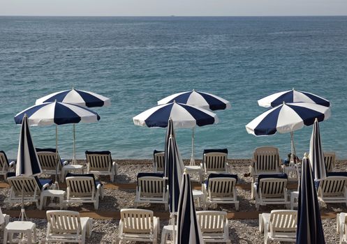 Beach with white and blue umbrellas near Promenade des Anglais in city of Nice, France.