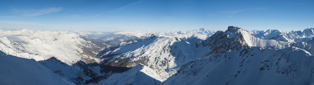 Panoramic view across snow covered alpine mountain range in alps on blue sky background
