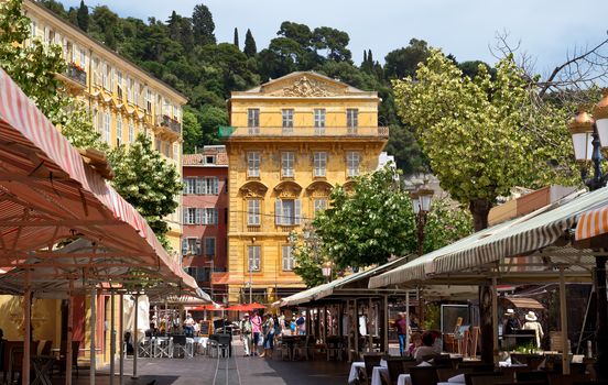 NICE, FRANCE - JUNE 6, 2014: Old building and a cafe in the Cours Saleya. The Cours Saleya is a place of outdoor restaurants, boutiques and a market.

Nice, France - June 6, 2014: Old building and a cafe in the Cours Saleya. The Cours Saleya is a place of outdoor restaurants, boutiques and a market. People are walking by street.