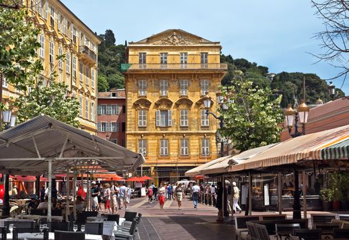 NICE, FRANCE - JUNE 6, 2014: Old building and a cafe in the Cours Saleya. The Cours Saleya is a place of outdoor restaurants, boutiques and a market.

Nice, France - June 6, 2014: Old building and a cafe in the Cours Saleya. The Cours Saleya is a place of outdoor restaurants, boutiques and a market. People are walking by street.