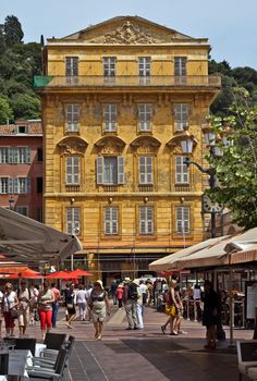 NICE, FRANCE - JUNE 6, 2014: Old building and a cafe in the Cours Saleya. The Cours Saleya is a place of outdoor restaurants, boutiques and a market.

Nice, France - June 6, 2014: Old building and a cafe in the Cours Saleya. The Cours Saleya is a place of outdoor restaurants, boutiques and a market. People are walking by street.