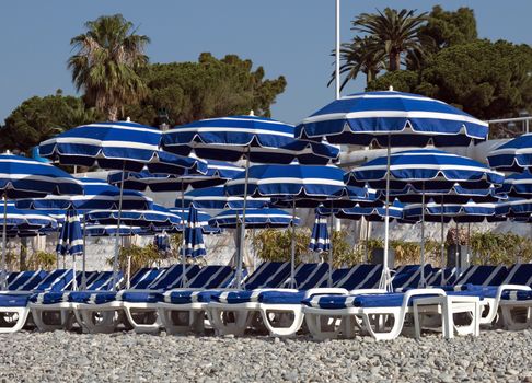 Beach with blue umbrellas near Promenade des Anglais in city of Nice, France.