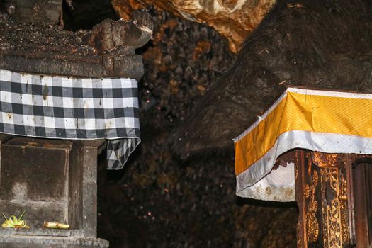 Altars at Pura Goa Lawah or Bat Cave Temple. Balinese Hindu temple, Klungkung, Bali, Indonesia. Some bats fly under a rock overhang. Colony of bats hanging from the ceiling and are waiting dark.