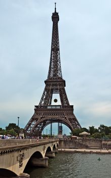 PARIS, FRANCE - JUNE 9, 2014: Eiffel tower and old bridge over Seine river. The Eiffel tower is the most visited monument of Paris.

Paris, France - June 9, 2014: Eiffel tower and old bridge over Seine river. The Eiffel tower is the most visited monument of Paris. People are walking across the bridge.
