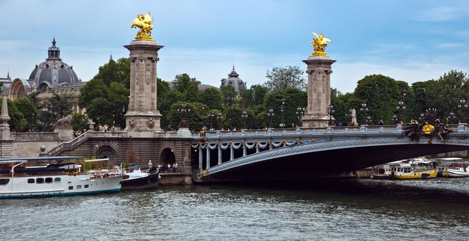 PARIS, FRANCE - JUNE 9, 2014: Pont Alexandre III, Paris, France. The bridge, with its Art Nouveau lamps, cherubs, nymphs and winged horses at either end, was built between 1896 and 1900. 

Paris, France - June 9, 2014: Pont Alexandre III, Paris, France. The bridge, with its Art Nouveau lamps, cherubs, nymphs and winged horses at either end, was built between 1896 and 1900. People are standing under a bridge and are walking by bridge.