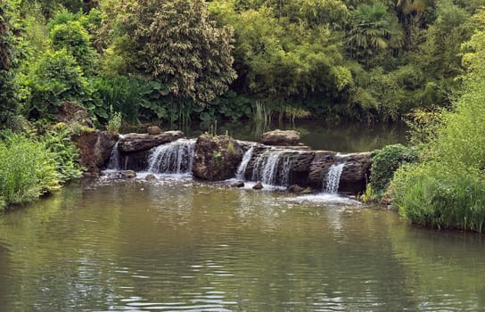 Small waterfall in a lush green forest in France.