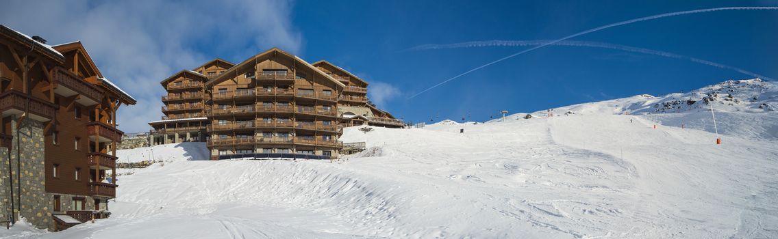 Panoramic view of snow covered piste in an alpine ski resort with apartment buildings on slope