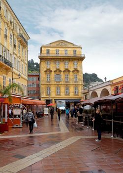NICE, FRANCE - APRIL 27: Old building and a cafe in the Cours Saleya on April 27, 2013 in Nice, France. The Cours Saleya is a place of outdoor restaurants and a market. 

Nice, France - April 27, 2013: Old building and a cafe in the Cours Saleya. People are walking and relaxing.
The Cours Saleya is a place of outdoor restaurants, boutiques and a market. 