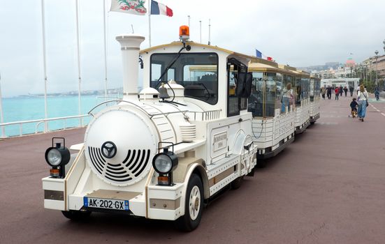 NICE, FRANCE - APRIL 27: White trackless train for sightseeing on the Promenade des Anglais on April 27, 2013 in Nice, France. People are walking along Promenade des Anglais.

Nice, France - April 27, 2013 : White trackless train for sightseeing on the Promenade des Anglais in Nice. People are walking along Promenade des Anglais.