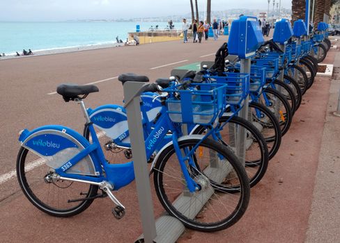 NICE, FRANCE - APRIL 27: Public Bicycles Sharing Station on April 27, 2013 in Nice, France. One of 120 stations in Nice. This service offers over 1200 self-service bicycles.

Nice, France - April 27, 2013: Row of public bikes for rent along the street. People are walking. Nice has 120 stations. This service offers over 1200 self-service bicycles. People are walking by Promenade.