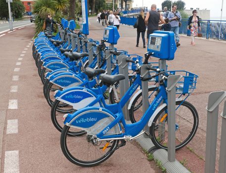 NICE, FRANCE - APRIL 27: Public Bicycles Sharing Station on April 27, 2013 in Nice, France. One of 120 stations in Nice. This service offers over 1200 self-service bicycles.

Nice, France - April 27, 2013: Row of public bikes for rent along the street. People are walking. Nice has 120 stations. This service offers over 1200 self-service bicycles.