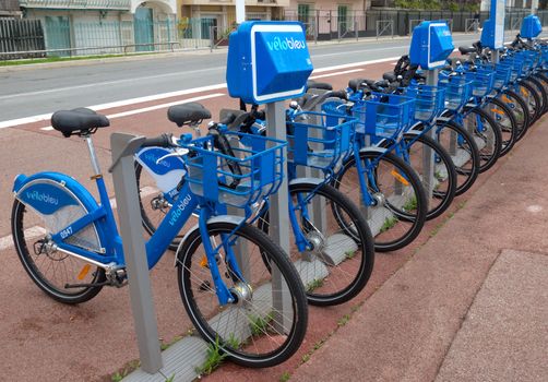 NICE, FRANCE - APRIL 27: Public Bicycles Sharing Station on April 27, 2013 in Nice, France. One of 120 stations in Nice. This service offers over 1200 self-service bicycles.

Nice, France - April 27, 2013: Row of public bikes for rent along the street. People are walking. Nice has 120 stations. This service offers over 1200 self-service bicycles. People take a bicycle.