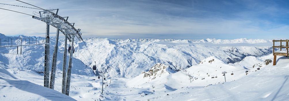 Panoramic view of a snow covered alpine mountain range with cable car ski lift over piste