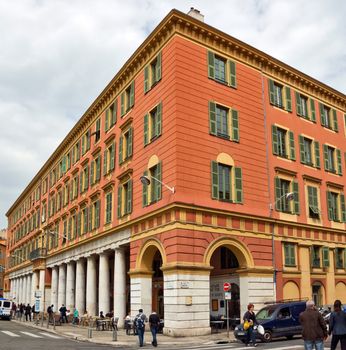 NICE, FRANCE - APRIL 30: The architecture of buildings on the Place Massena on April 30, 2013 in Nice, France. The square is bordered by red ochre buildings of Italian architecture.

Nice, France - April 30, 2013: The architecture of buildings on the Place Massena. The square is bordered by red ochre buildings of Italian architecture. People are walking by street.