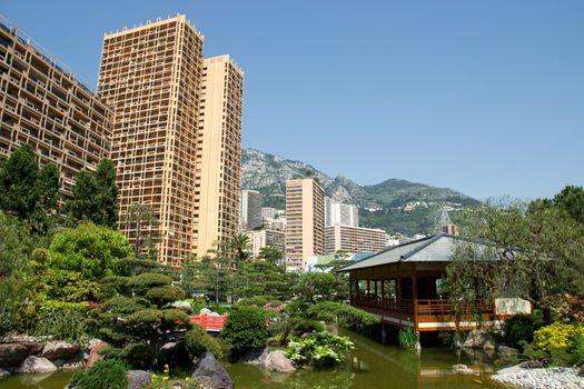 Japanese garden of Monaco, with a japanese house and a pond and Monte Carlo buildings behind. 