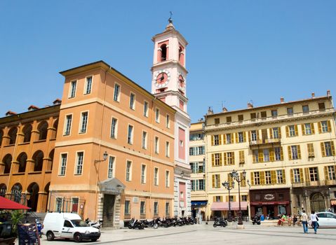NICE, FRANCE - MAY 2: Square - Place du Palais on May 2, 2013 in Nice, France. There are the Palace of Justice and the Palace Rusca with clock tower. 

Nice, France - May 2, 2013: Square - Place du Palais is one of more famous squares of Nice. There are the Palace of Justice and the Palace Rusca with clock tower. Today, the Place du Palais is alive day and night. Often, groups of youths will hangout on the steps leading to the Palais de la Justice. Concerts, films, and other major public events frequently occur in this space.
On the photo people are resting, meeting and walking.