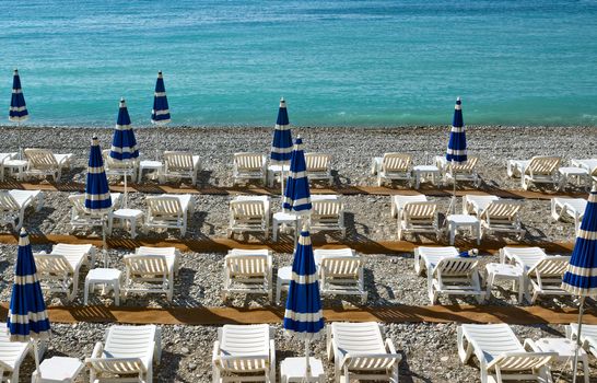 Beach with blue umbrellas near Promenade des Anglais in city of Nice, France.