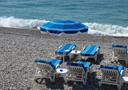 Beach with blue umbrella near Promenade des Anglais in city of Nice, France.