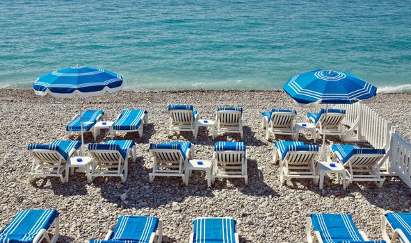 Beach with blue umbrellas near Promenade des Anglais in city of Nice, France.