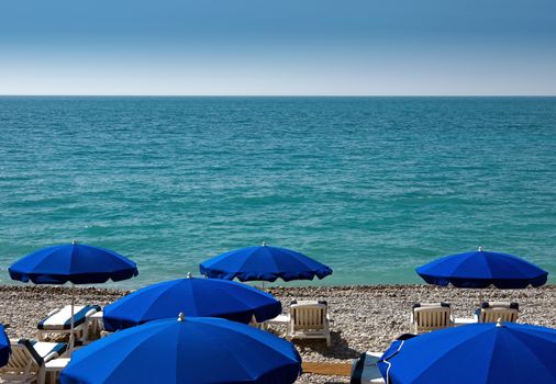 Beach with blue umbrellas near Promenade des Anglais in city of Nice, France. 