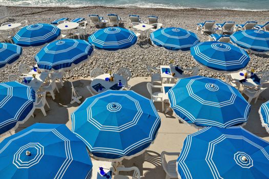 Beach with blue umbrellas near Promenade des Anglais in city of Nice, France.