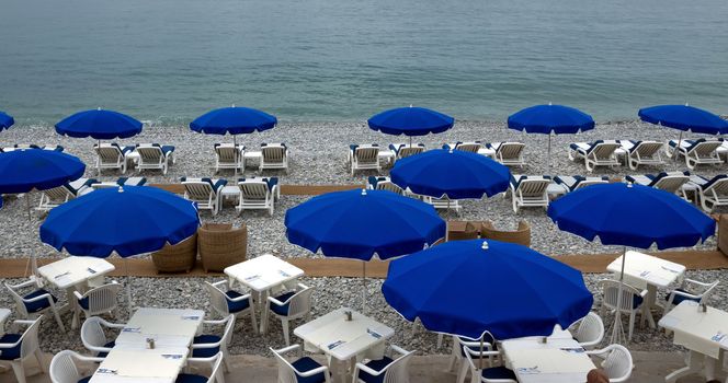 Beach with blue umbrellas near Promenade des Anglais in city of Nice, France. 