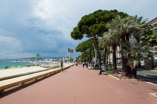 CANNES, FRANCE - MAY 6: Pedestrians walking on the famous "La Croisette" Boulevard on May 6, 2013 in Cannes, France. It is a symbol of the Cote d'Azur.

Cannes, France - May 6, 2013: Pedestrians walking on the famous "La Croisette" Boulevard. It is a symbol of the Cote d'Azur.