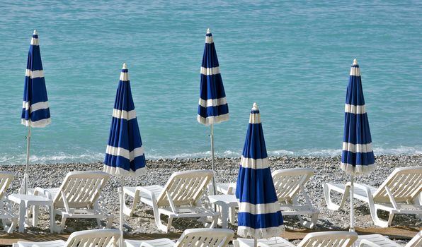 Beach with blue umbrellas near Promenade des Anglais in city of Nice, France.