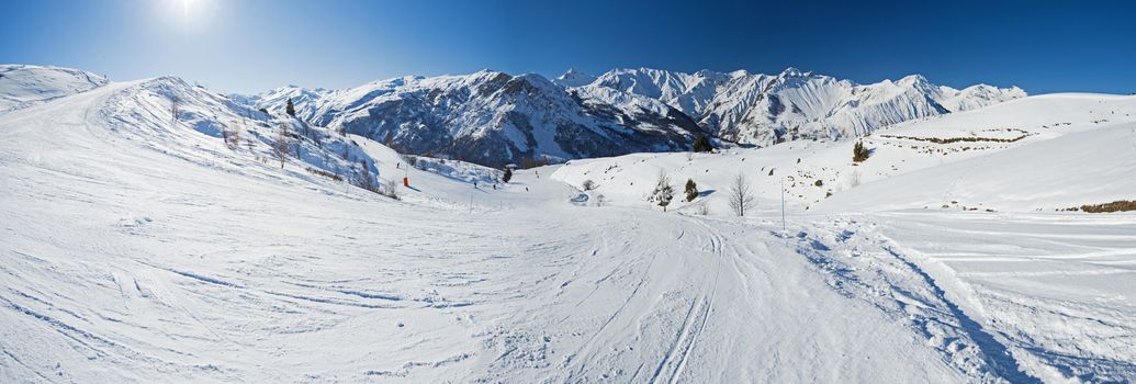 Panoramic landscape view down valley with ski slope piste in winter alpine mountain resort