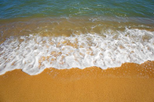 Water waves on the golden beach in sunny day