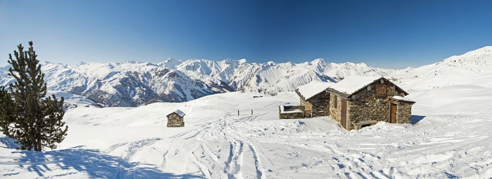 Panoramic view of snow covered mountains in an alpine ski resort with stone building on remote slope