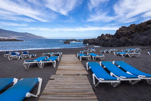 Blue sunbeds and black sand beach at Los Cancajos. La Palma, Canary Island, Spain.