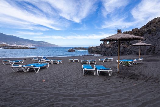 Blue sunbeds and black sand beach at Los Cancajos. La Palma, Canary Island, Spain.